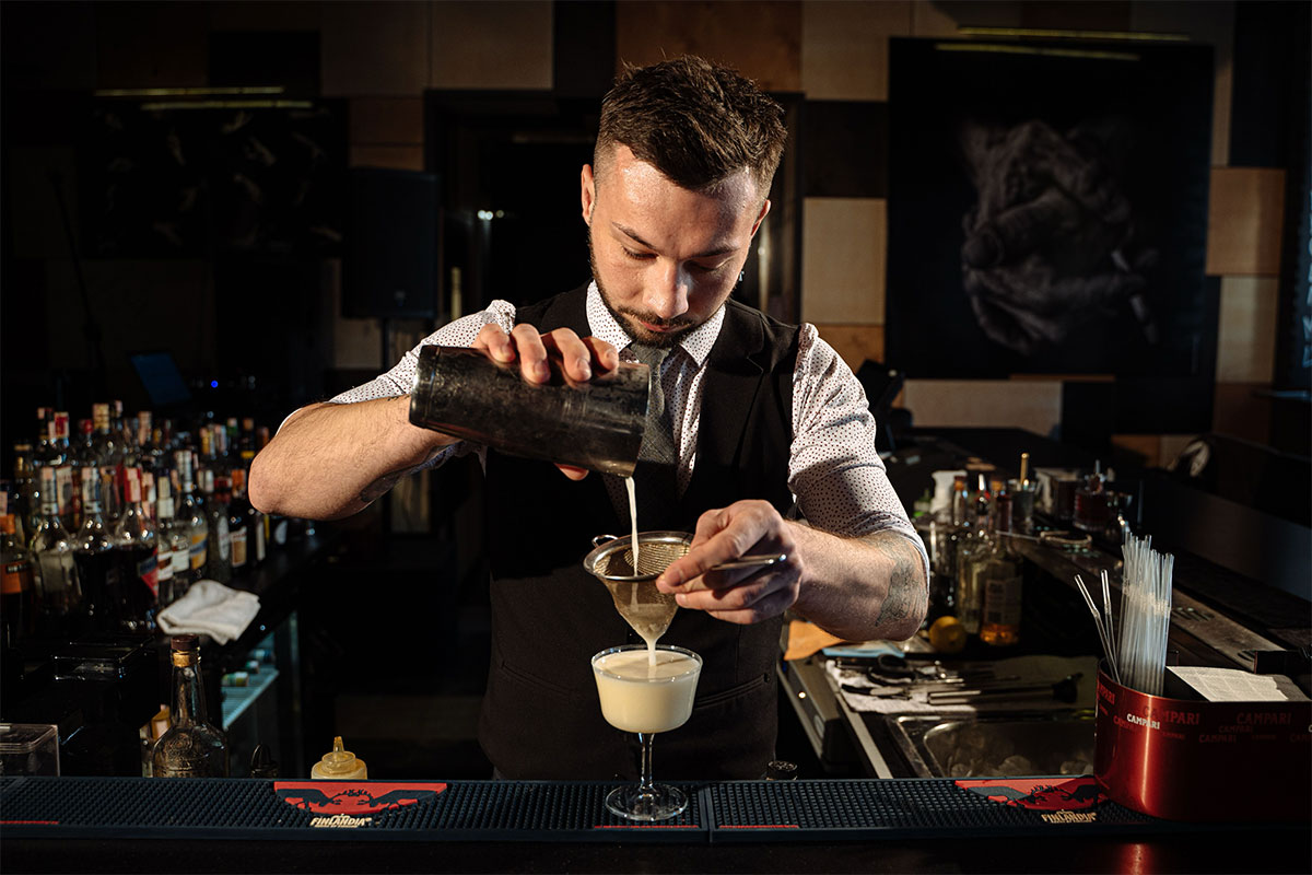 bartender preparando coctel con técnica interior bar elegante
